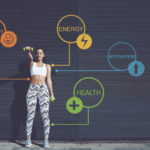 Photograph of fit woman in front of wall with health and wellness signs to illustrate, "Photograph of fit woman in front of wall with health and wellness signs to illustrate, "How A Ketogenic Diet Benefits Your Body And Mind".